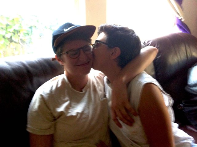 raquel kissing meg on the cheek, sitting on a couch