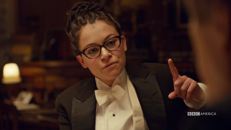 Cosima (still in her tux) holds up a finger mid-explanation