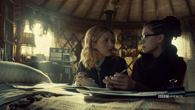 Delphine and Cosima kneel by the bed to talk science