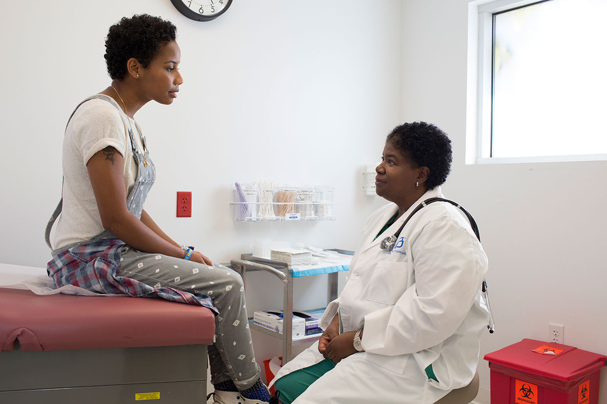 Woman sitting on the exam table, talking with her doctor.