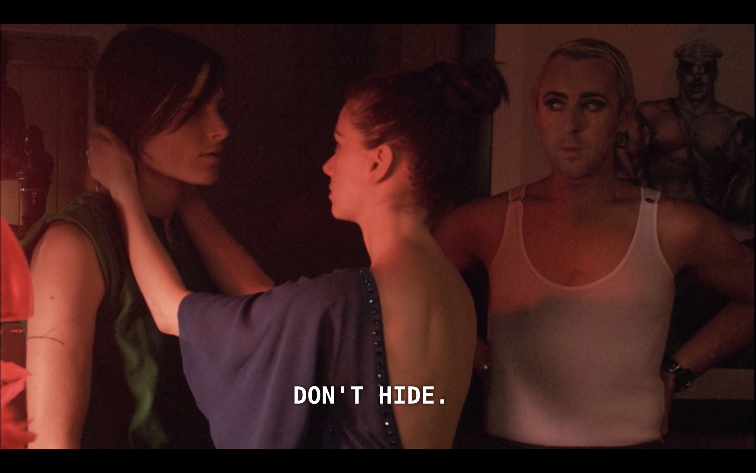 Billie (wearing a white tank top), looks at Jenny (wearing a blue dress) who is holding Max's (wearing a green tank top) face in her hands. Jenny says to Max, "Don't hide."