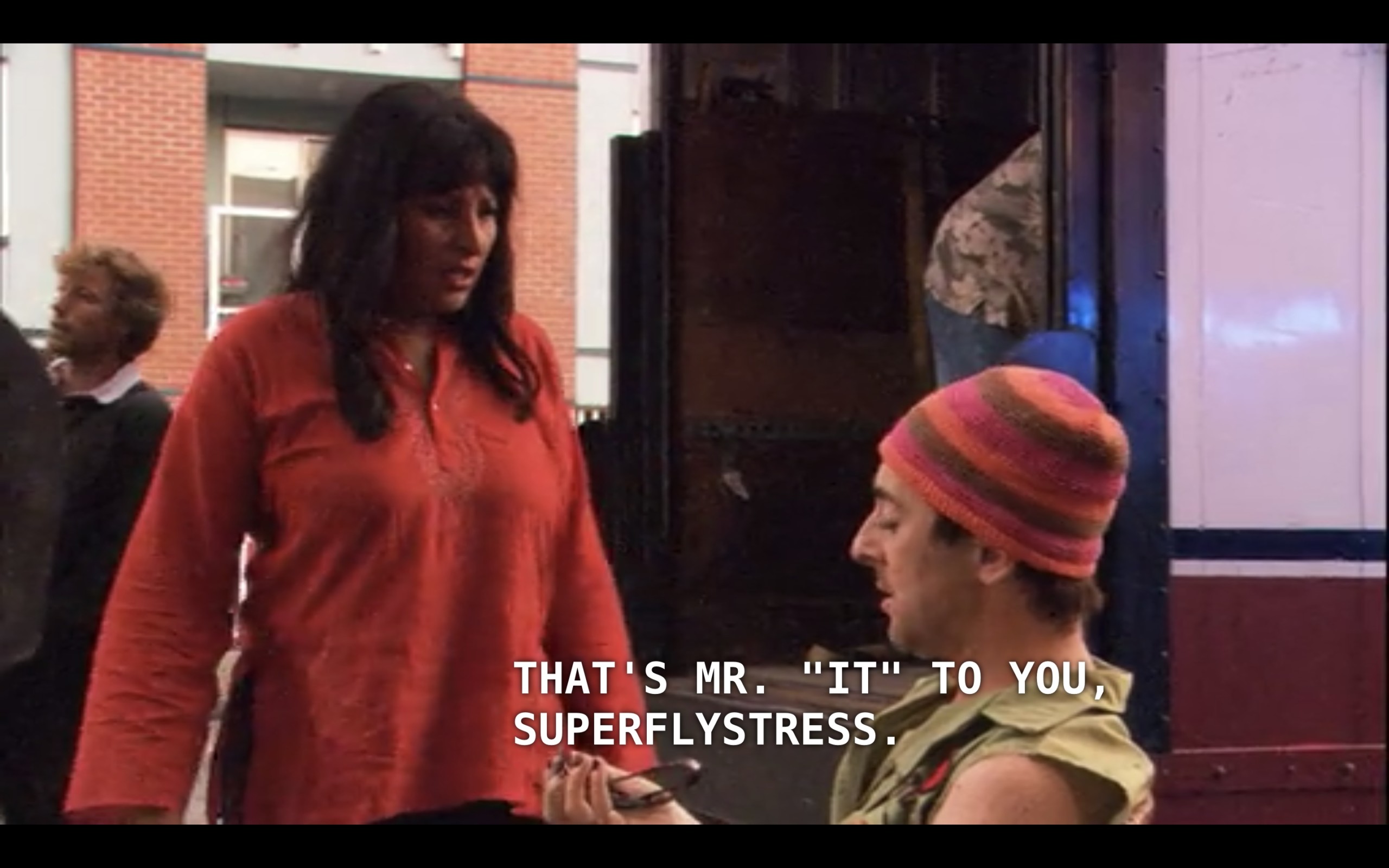 Kit (wearing a red shirt) is outside with Billie (wearing a green vest and a pink-and-brown striped beanie). Billie says, "That's Mr. 'It" to you, superflystress."