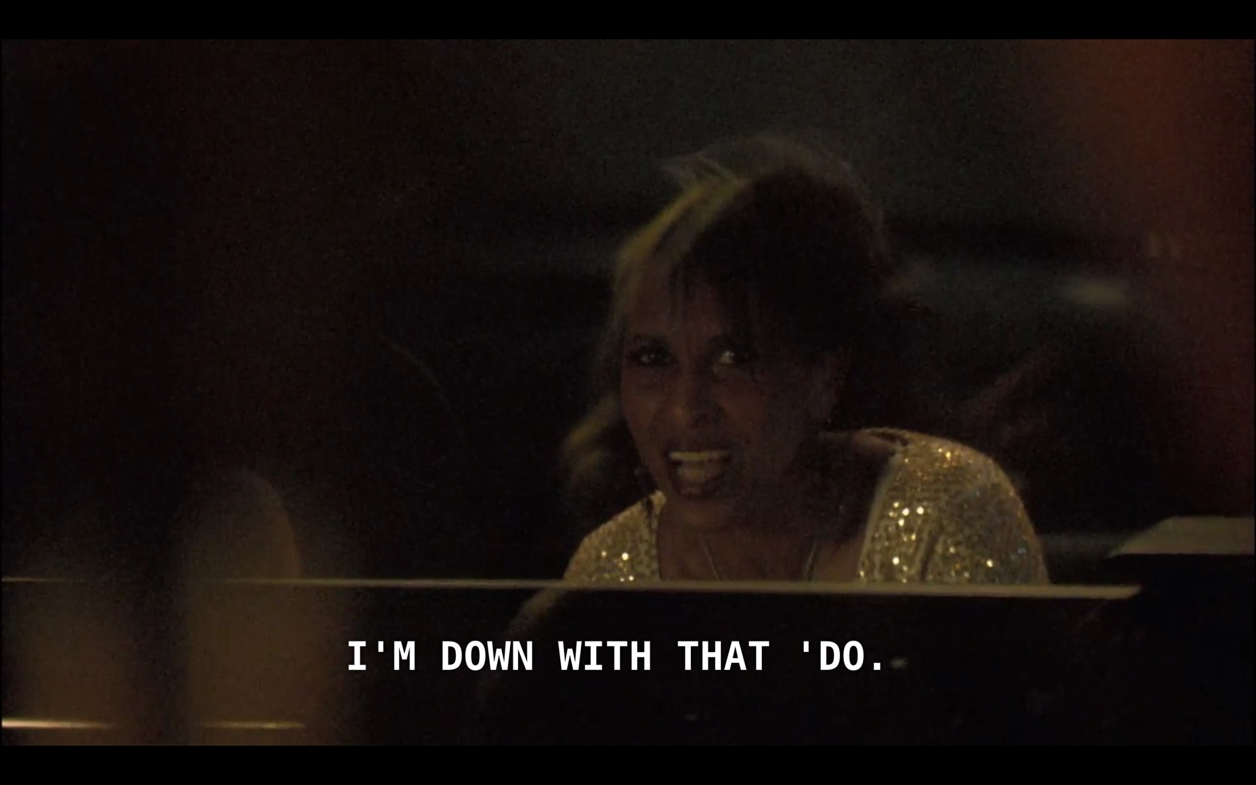 A woman wearing a gold sequins top sits in a recording studio. "I'm down with that 'do"
