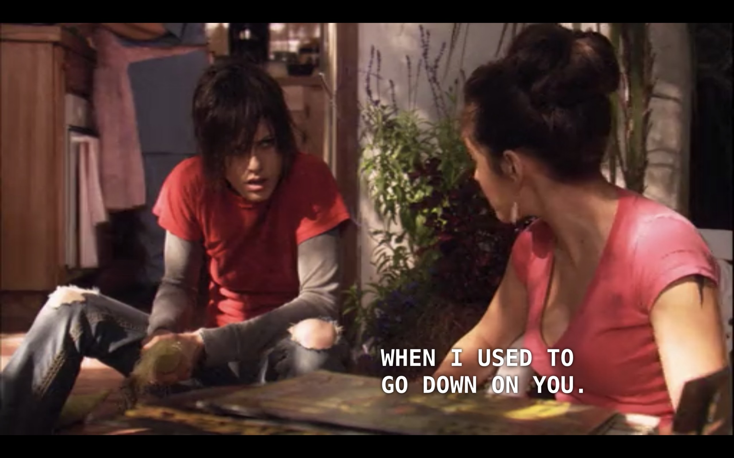 Carmen (wearing a pink top) and Shane (wearing a red t-shirt) are sitting on the floor at Carmen's family's house looking at records. Carmen says to Shane, "Back when I used to go down on you."