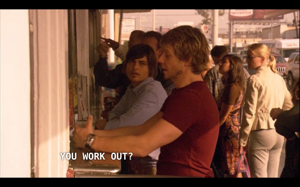 Tim (wearing a red t-shirt) and Max (wearing a blue button-up) stand at an outdoor bar. Max asks, "You work out?"