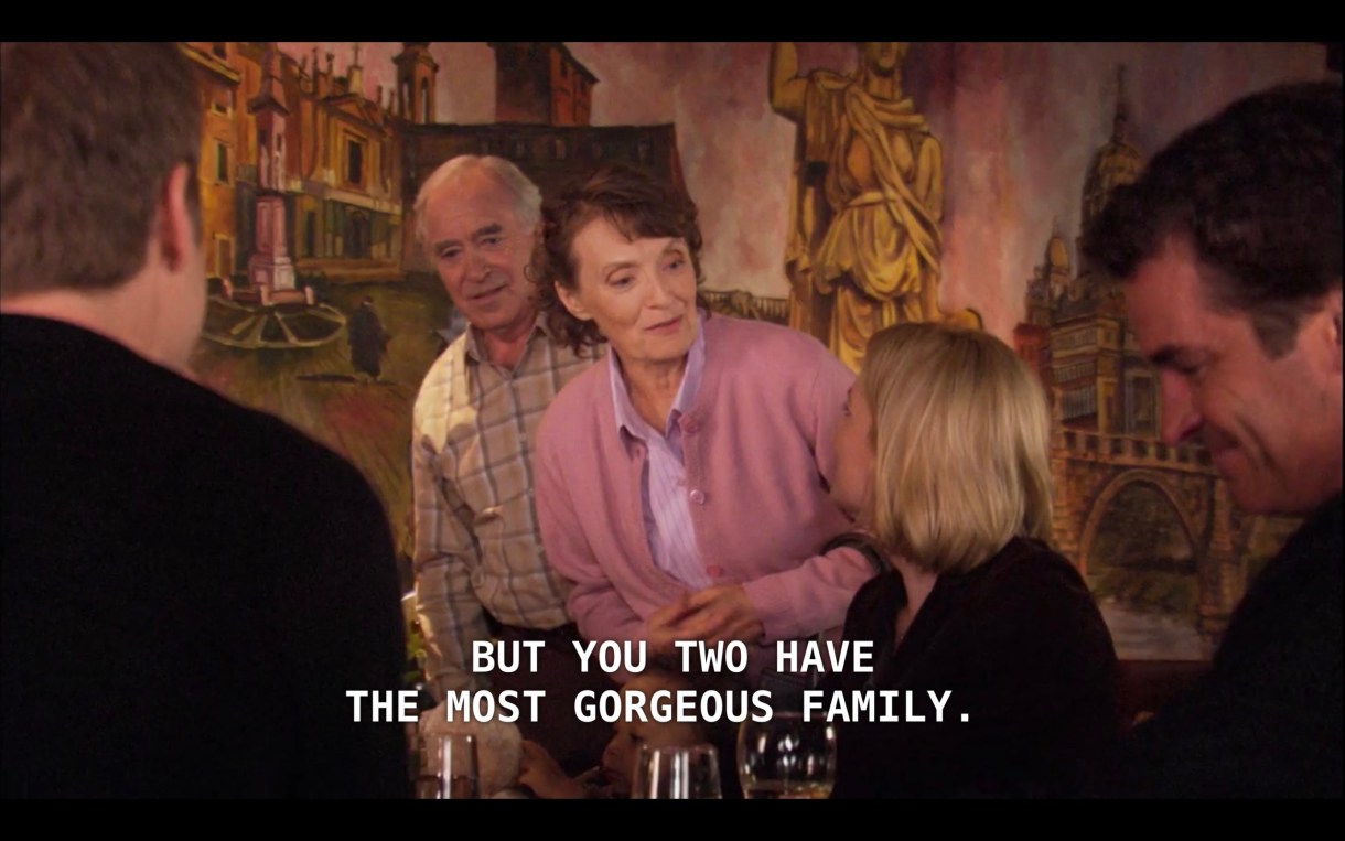 An older man (wearing a brown plaid shirt) and woman (wearing a pink sweater set) approach Tina and Henry at a restaurant. The woman says, "My husband and I have been sitting watching you, but you two have the most gorgeous family."