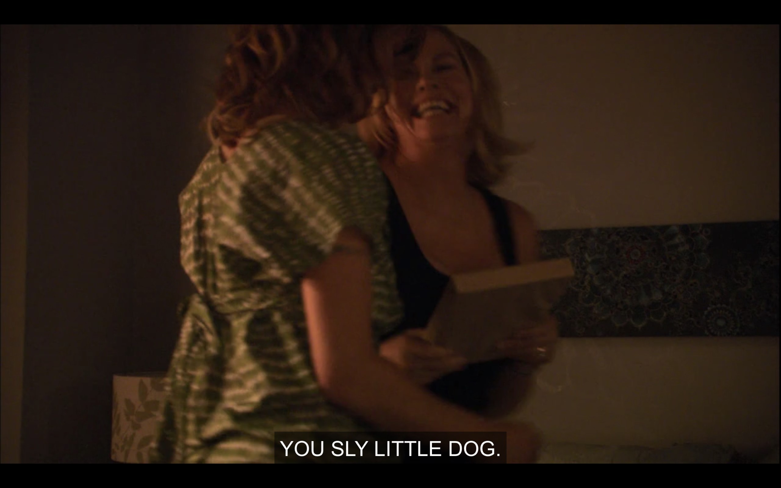 Phyllis and Alice in a dimly-lit room. Phyllis has a book in her hands. Alice says, "You sly little dog."