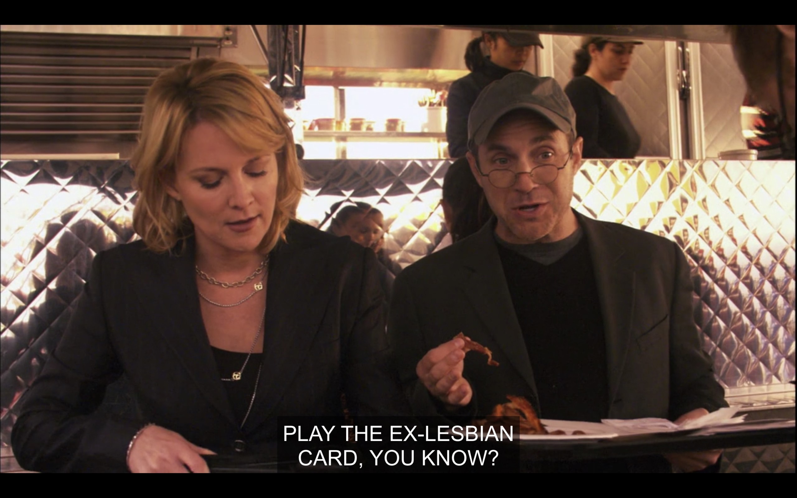Outside a trailer on set that serves food, Tina and Aaron are filling their plates and talking. Aaron says, "Play the Ex-Lesbian card, you know?'