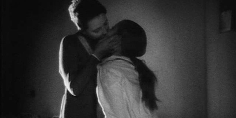 A still from Mรคdchen in Uniform. A woman bends down to kiss a girl wearing white pajamas.