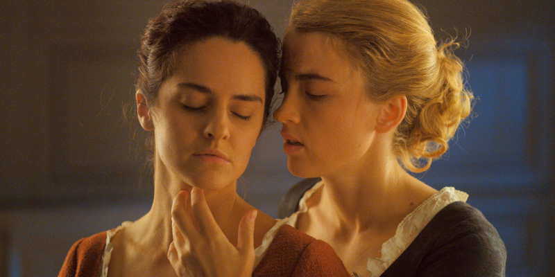 A still from Portrait of a Lady on Fire. Two women in 18th century dresses embrace in golden light.