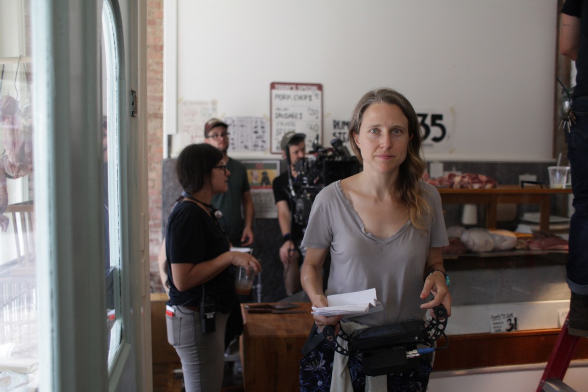 A candid photo of director Josephine Decker facing the camera on set, holding a script in hand