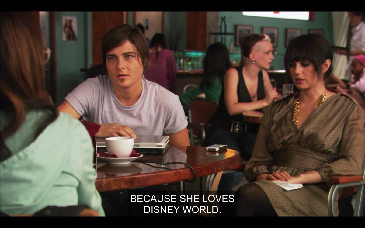 Max and Jenny are sitting at a table at The Planet with Adele, whose back is to the camera. "Because she loves Disney World."