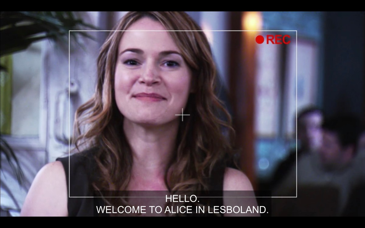 Looking through the camera at Alice, who is happy and saying "Hello, Welcome to Alice in Lesboland." They're at The Planet.