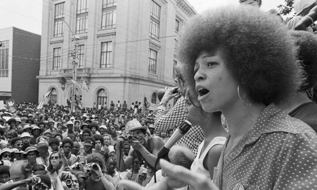 Angela Davis speaking into a microphone in front of a large crowd.