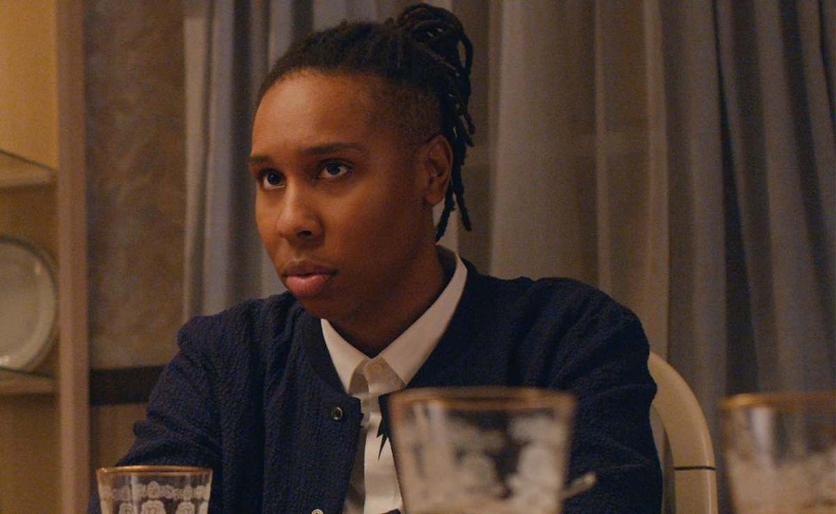 Lena Waithe in Master of None during the second season, she has dreadlocks pulled back into a high ponytail and a collard shirt underneath a bomber sports jacket. It is thanksgiving dinner and she is sitting at her mom's dinner table.