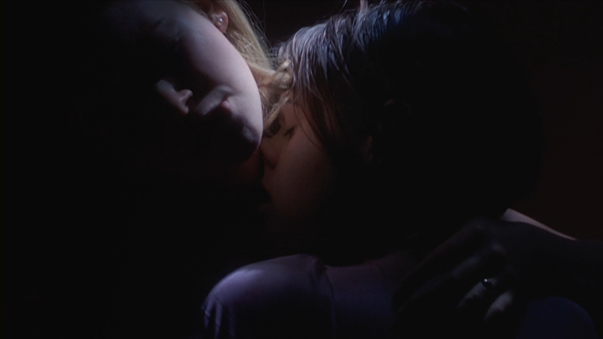 Clea Duvall kisses Natasha Lyonne's neck in low lighting.
