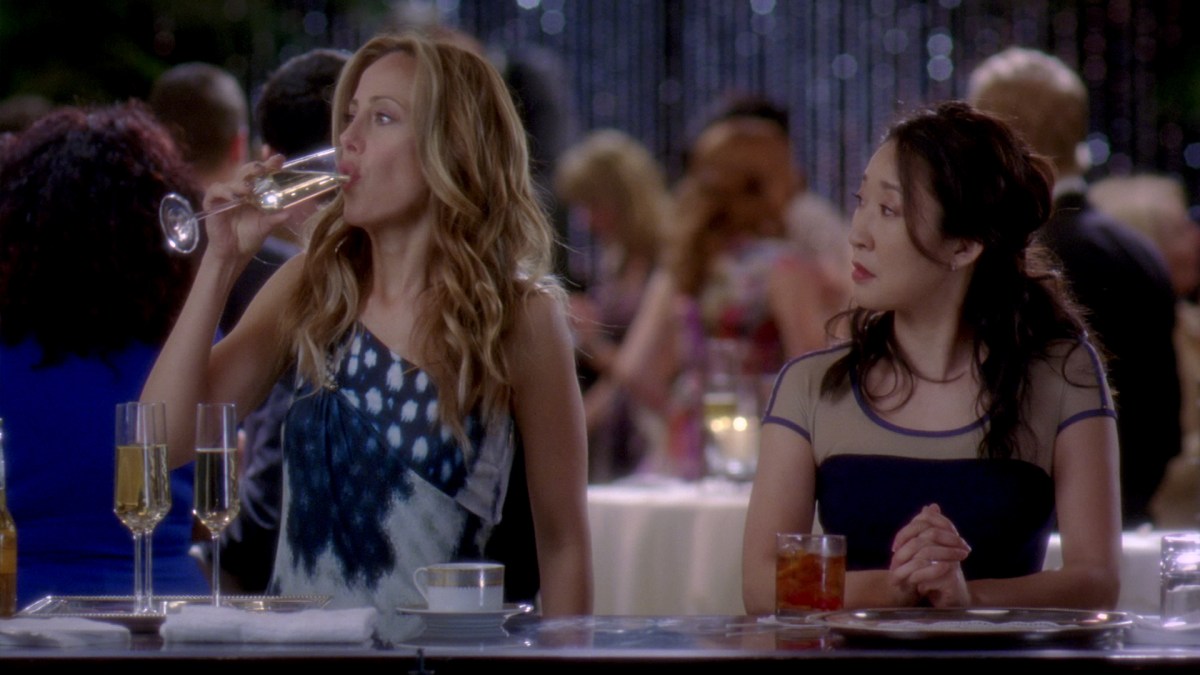 Still of Teddy and Cristina from Grey's Anatomy. Teddy is drinking champagne, Cristina is looking at her as she does.