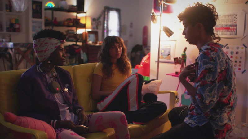 Victoria talks to Honeybear and Ash who are next to each other on a yellow couch