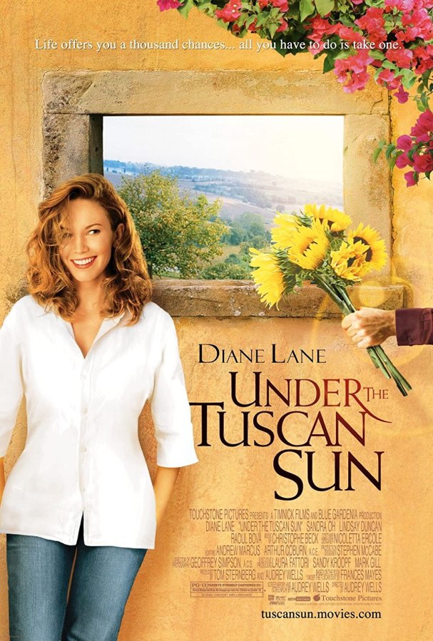 A woman leans against a stucco wall with a window in it while a hand offers her sunflowers from off-screen. The cover for Under the Tuscan Sun.