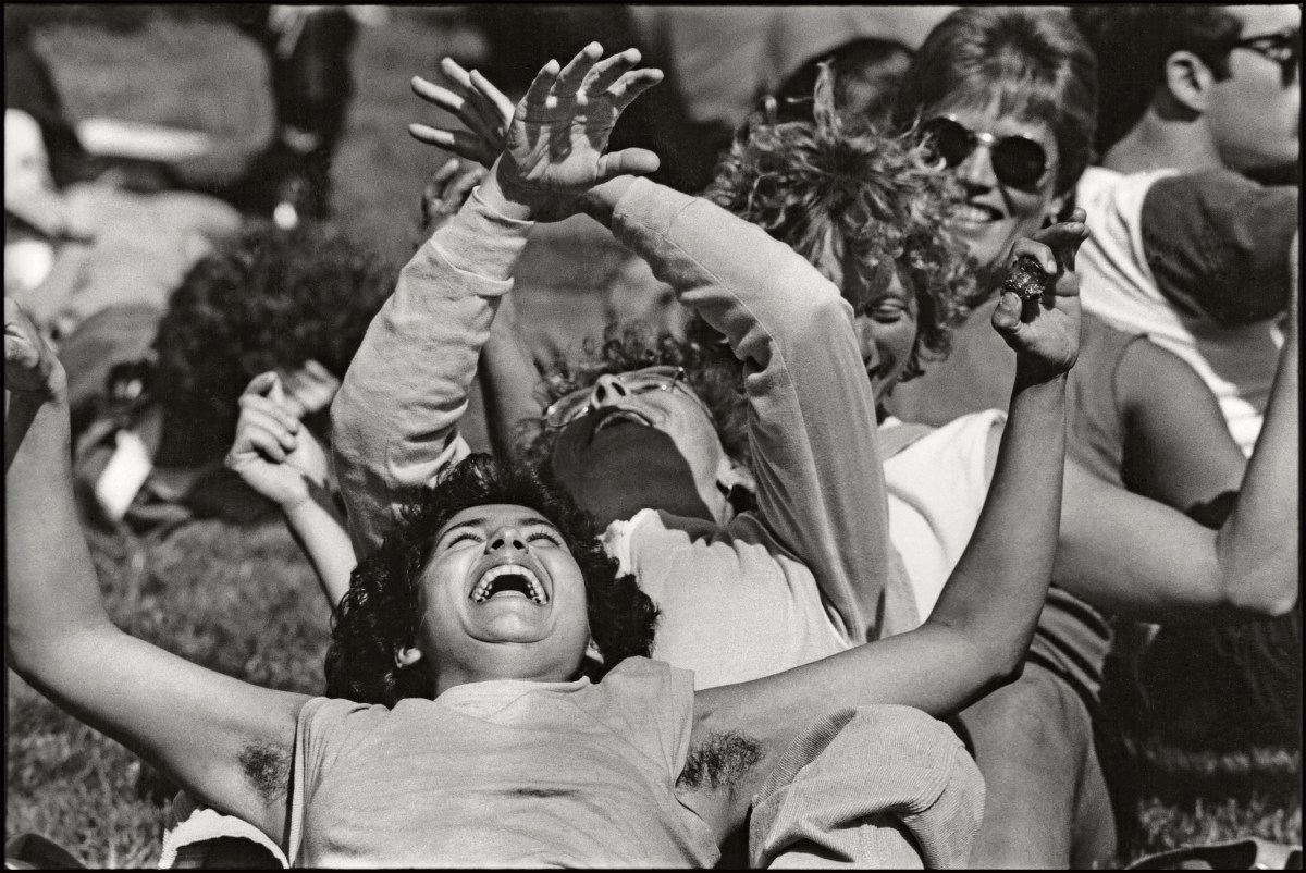 View of a line of women as they lie back in another's laps, laughing as they raise their arms outside the Civic Center 