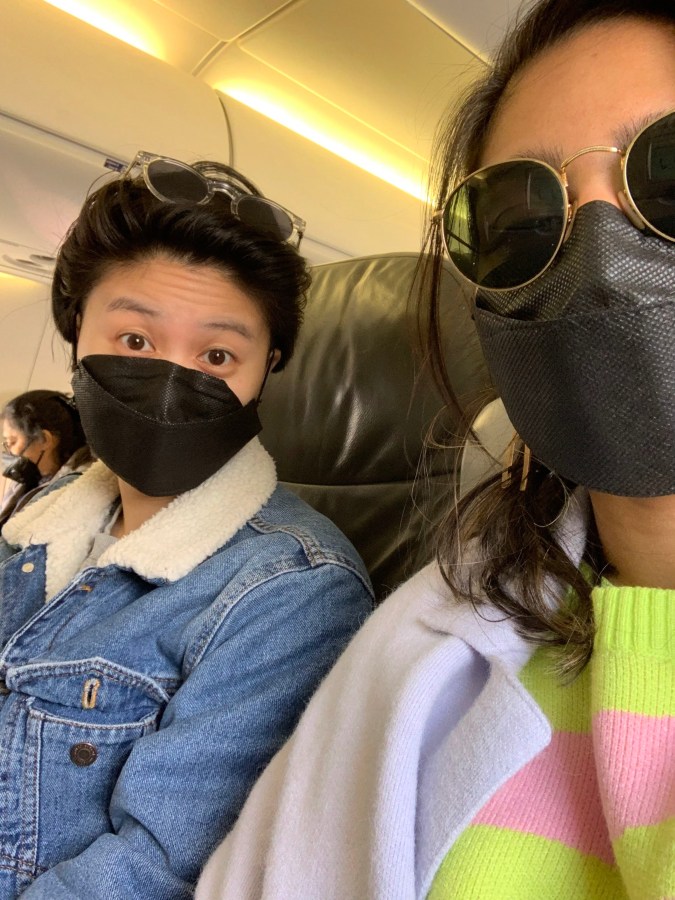 Here Gerrie and Ashni sit on a plain, wearing masks and sunglasses. Gerrie's sunglasses are on top of their head