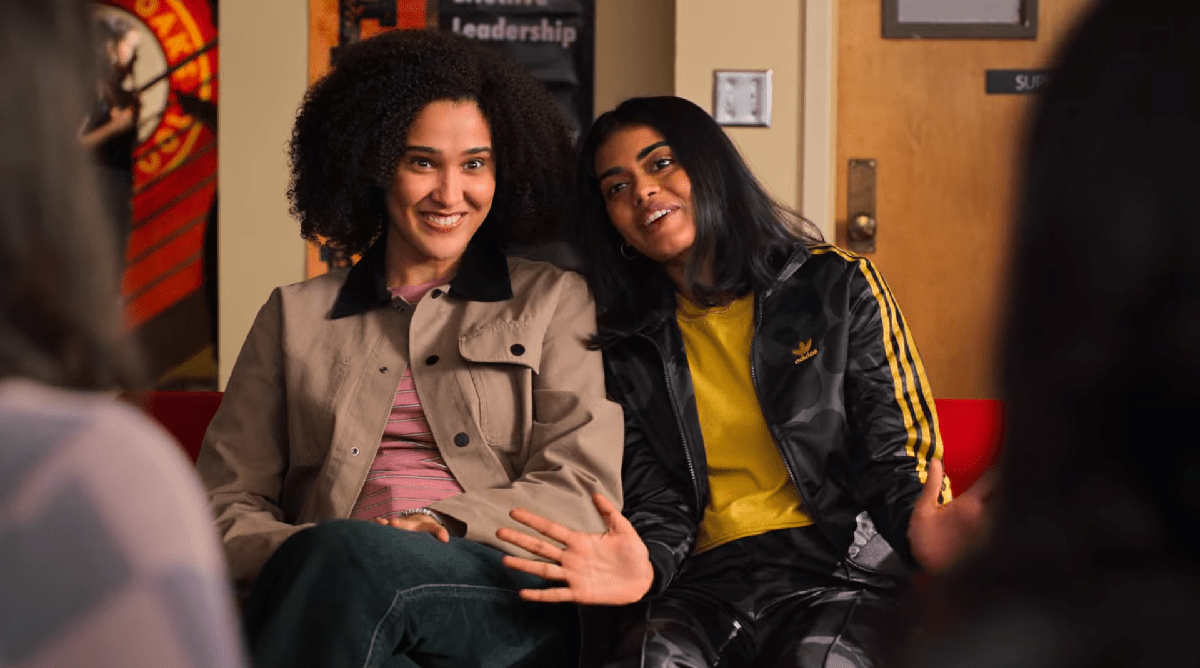 Fabiola and Aneesa sit with their shoulders pressed, smiling. Aneesa leans into Fabiola with her hands outstretched. 