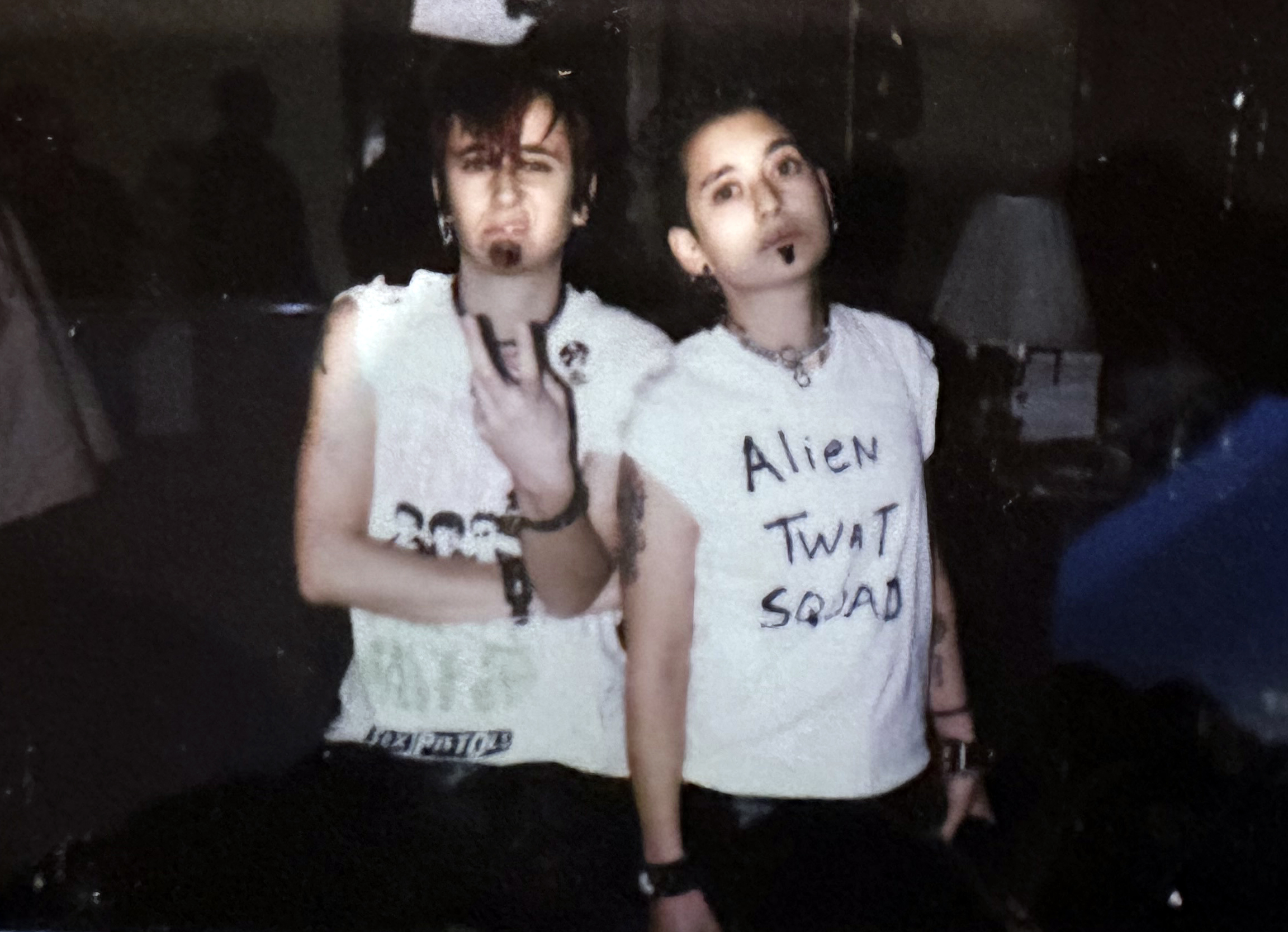 Tracy and Mia are dressed in drag as the sex pistols or also "alien twat squad" which is also written on Tracy's shirt. They've both drawn soul patches onto their faces and have styled their hair to look masculine.