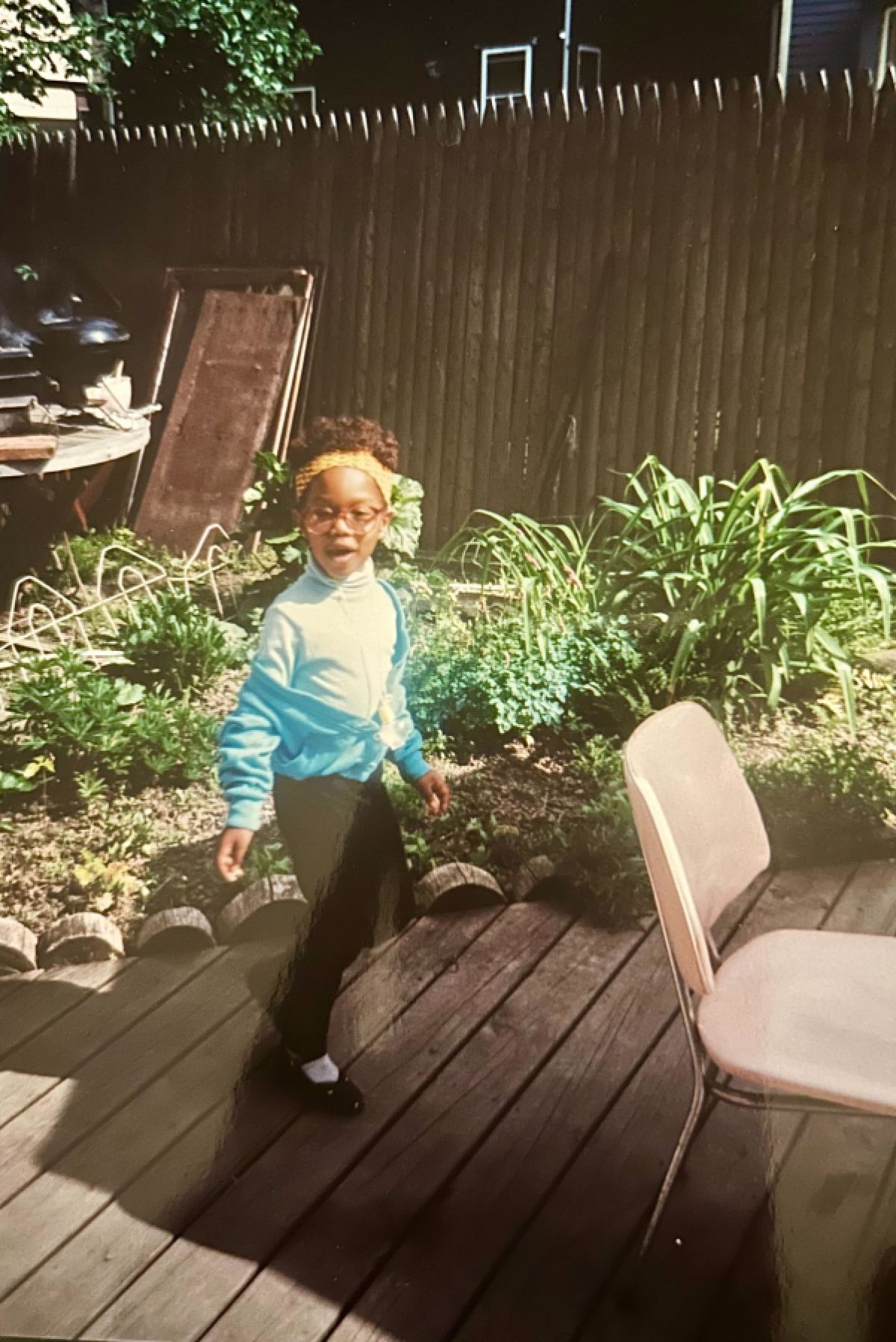 Carmen is about six years old and in a yellow headband, red glasses, and turquoise blue sweater set with black leggings, she's running around her Aunt Lorna's backyard.