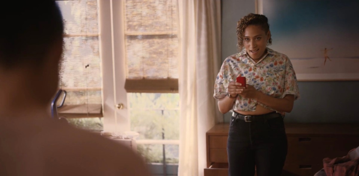 Sophie in a button-up short sleeved floral crop top and black jeans, holding an open jewelry box in amazement