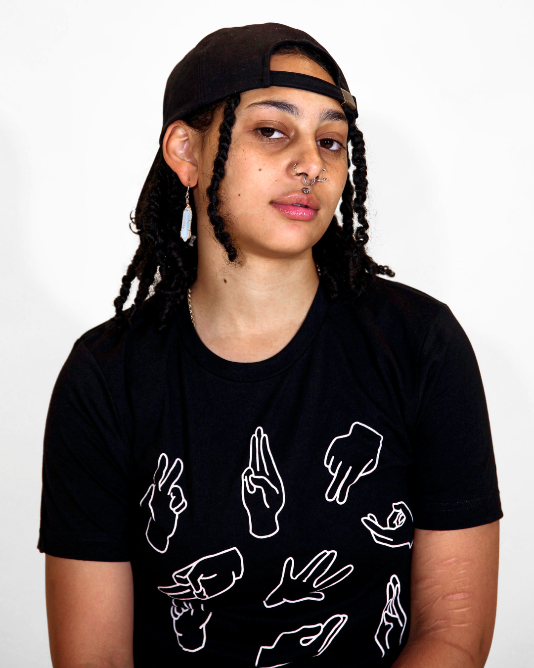 Model Grey is wearing the Fisting 101 Black Tee in size S. They are 5'4" and their bra size is 32D. The tee is black with line drawings of hand positions for sex in white color. The illustration was designed by Ren Strapp.