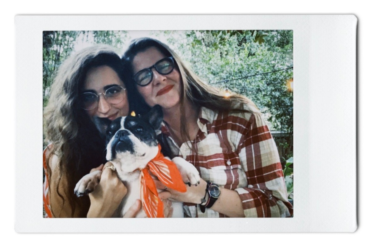 Kayla and Kristen hold up Lola, the black and white French bulldog