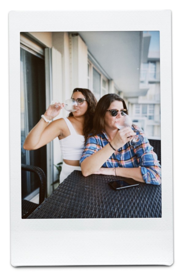 Kayla and Kristen hold large wine glasses and drink on their balcony in Miami