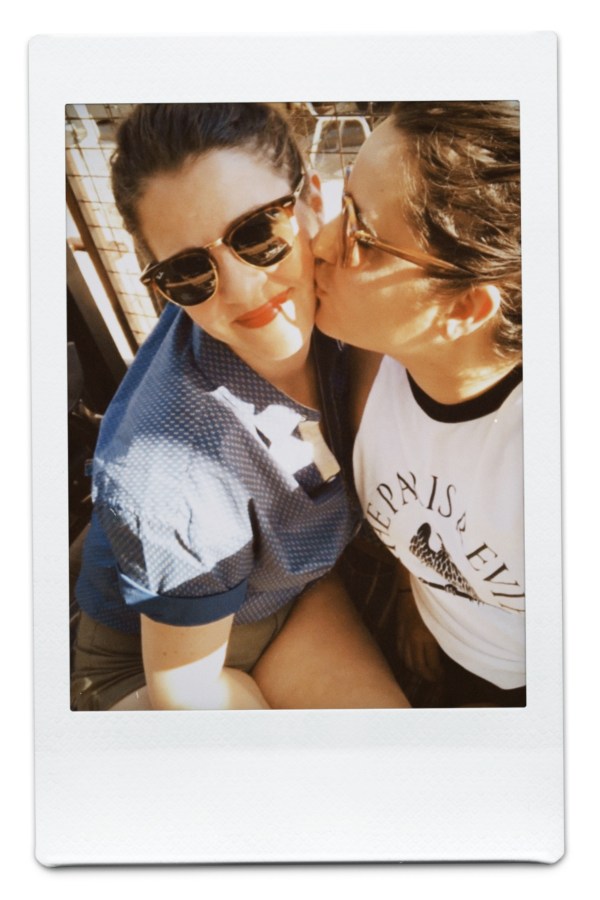 Kayla kisses Kristen on the cheek. They're both wearing sunglasses and sitting in the sun