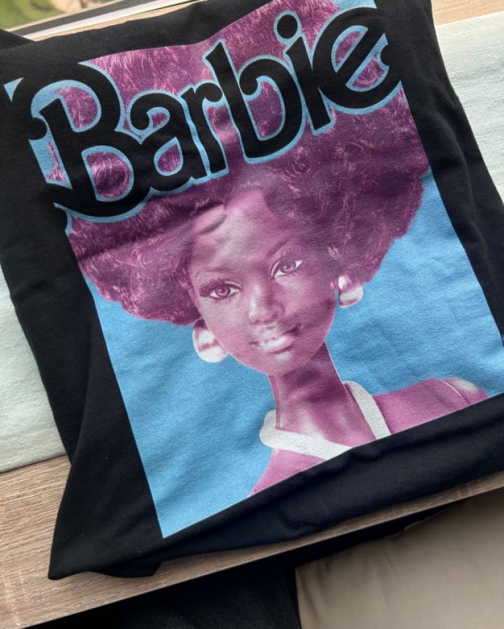 A folded up black t-shirt with a Black barbie from the 1960s and the Barbie logo.