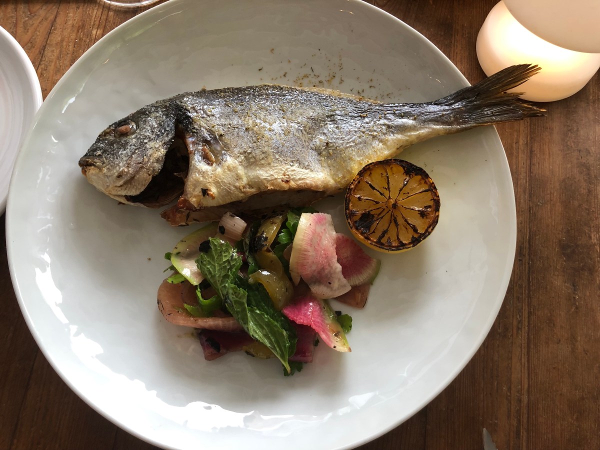 a whole grilled fish on a plate with pickled veggies and a grilled lemon