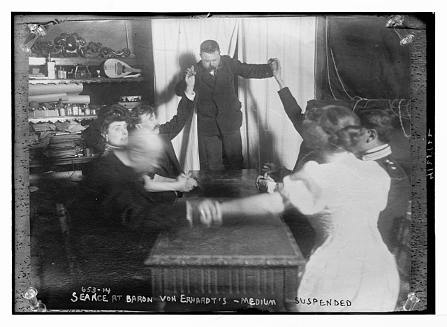 a table of victorians are having a seance and a guy is jumping back