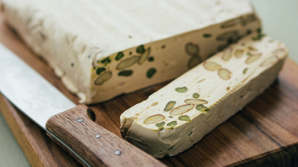 A full torrone with one piece cut off on a cutting board with a knife next to it