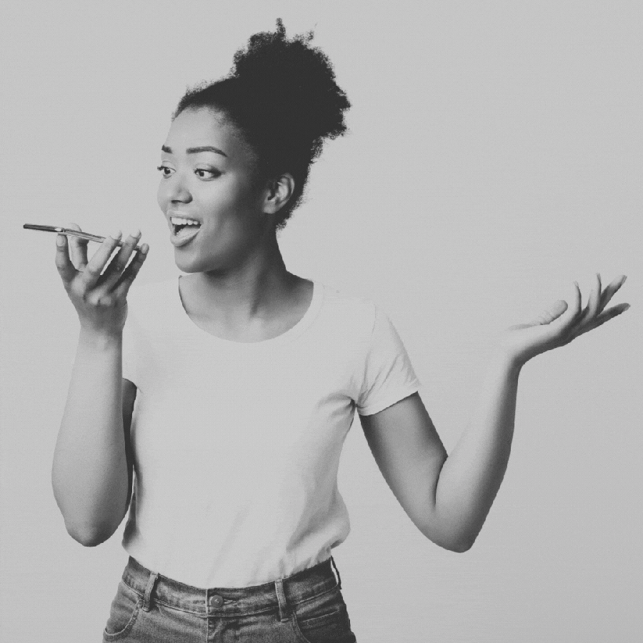 a GIF of a Black woman in black and white giving a voice memo into a cell phone. cassette tapes in purple, pink and orange appear above her open hand because Sagittarius' bad new year's resolution for their zodiac sign is to keep a ton of unhinged voice memos