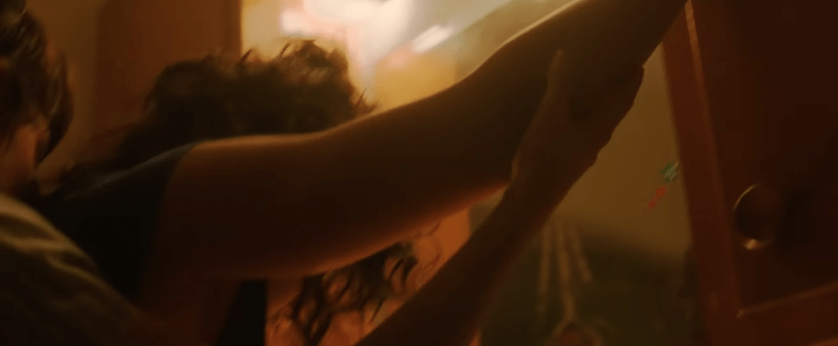 Katy M. O'Brian leaning against a wall and being kissed from behind by Kristen Stewart in the Love Lies Bleeding trailer
